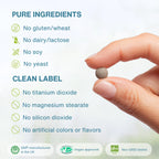 A close-up of a hand holding a small round supplement tablet against a soft light background, with text listing pure ingredients and clean label claims such as no gluten, wheat, dairy, lactose, soy, yeast, titanium dioxide, magnesium stearate, silicon dioxide, and artificial colors or flavors.